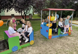 Dzieci siedzą w nowych wagonikach placu zabaw